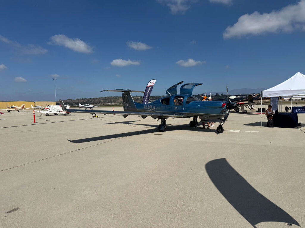 A blue single-engine airplane with its gull-wing doors raised